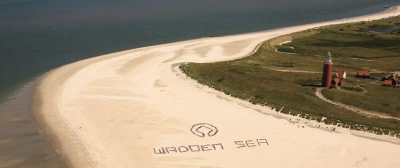 Aerial view on beach next to lighthouse with group of people forming letters 'WADDEN SEA' © Pieter de Vries.