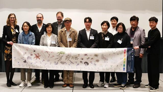 A group of people on a stage holding an educational banner with Wadden Sea plants and animals. © Young-Nam Kim/ KOEM.